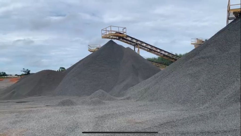 Montes de minério acinzentado extraído, com braços mecânicos de máquinas ao fundo.