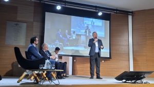 Em um pequeno palco, o diretor da AGEMS Matias Soares faz uma apresentação sobre a nova Câmara da ABAR de I.A, Inovação Tecnológica e Mudança Climática, acompanhada por outros três homens integrantes do painel temático.