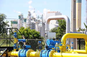Em primeiro plano. close em tubulação de distribuição da MSGÁS, nas cores azul e amarelo; ao fundo, instalação industrial.