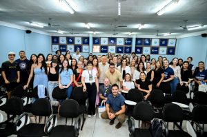 Grupo de mulheres da AGEMS, estudantes e instrutores da UNIGRAM posam com presidente Carlos Alberto no auditório.